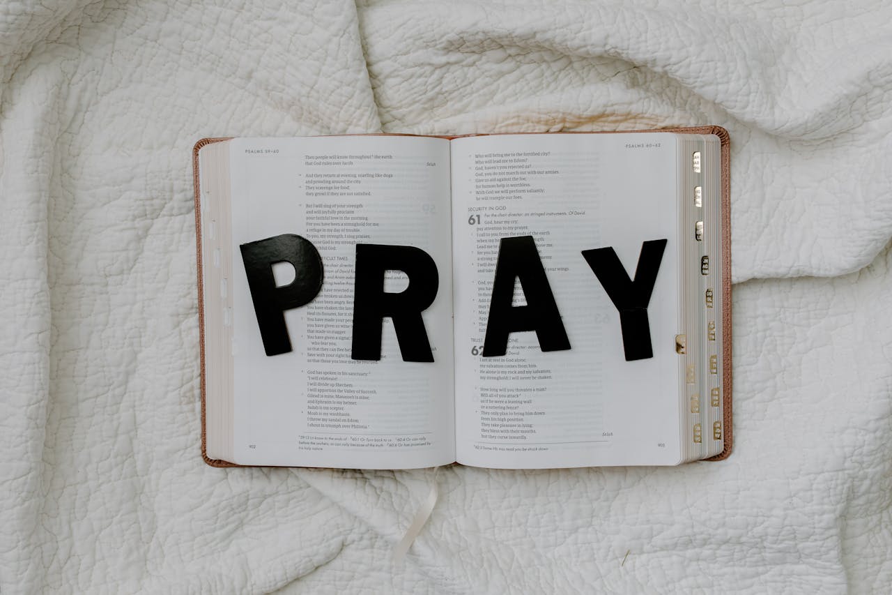 Open Bible with black letters spelling 'PRAY' on a white quilted fabric background.